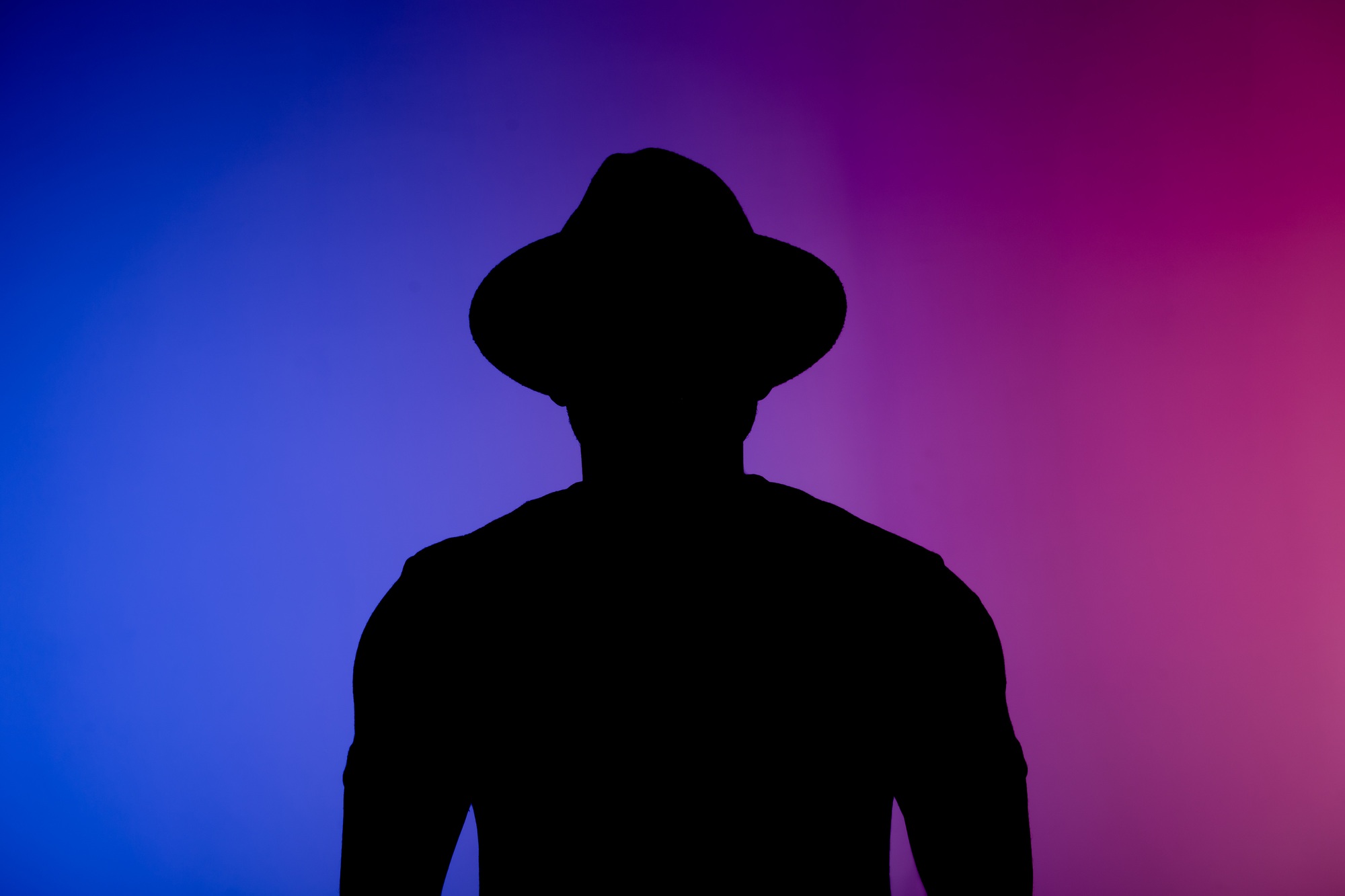 Silhouette head of sad african american man in hat on colourful neon isolated background - incognito